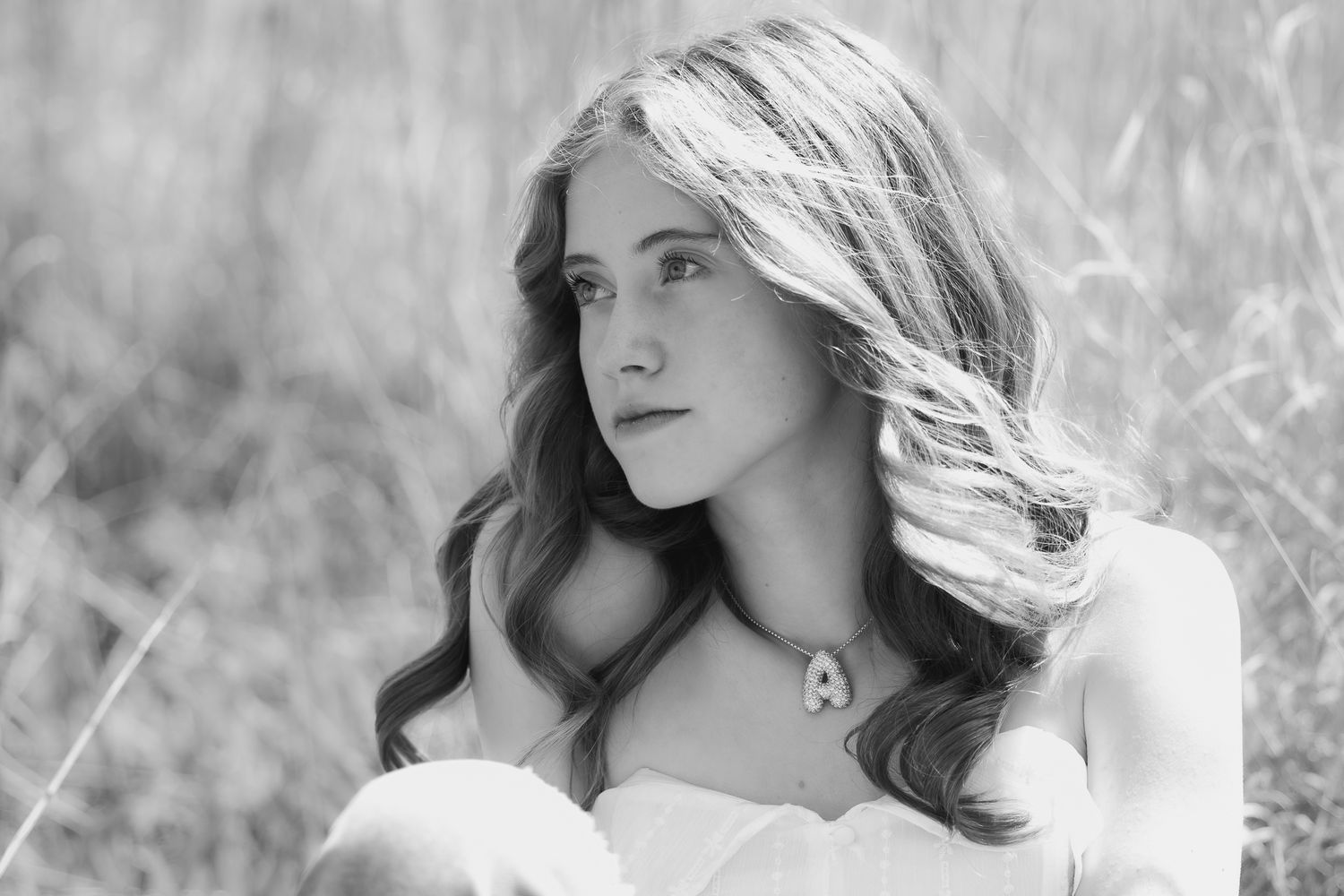 Black and white portrait of a woman with flowing hair in a white dress against a blurred nature background.