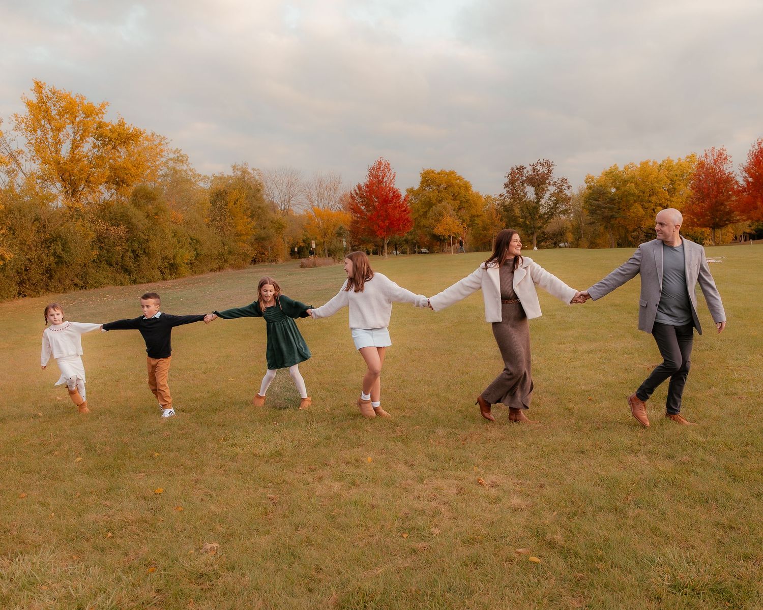 People spread out in line holding hands across autumn field at sunset.