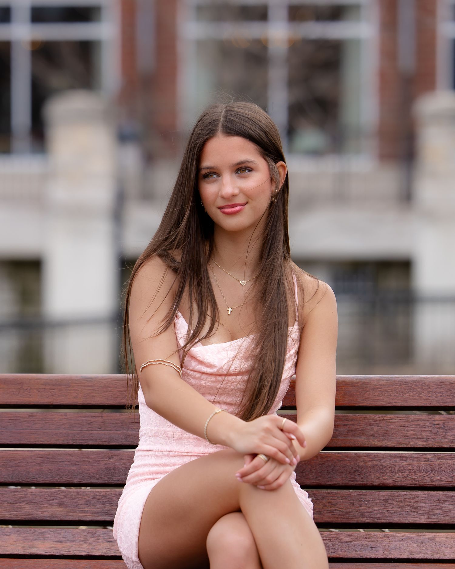 A person in a pink dress sitting on a wooden bench in an outdoor setting.