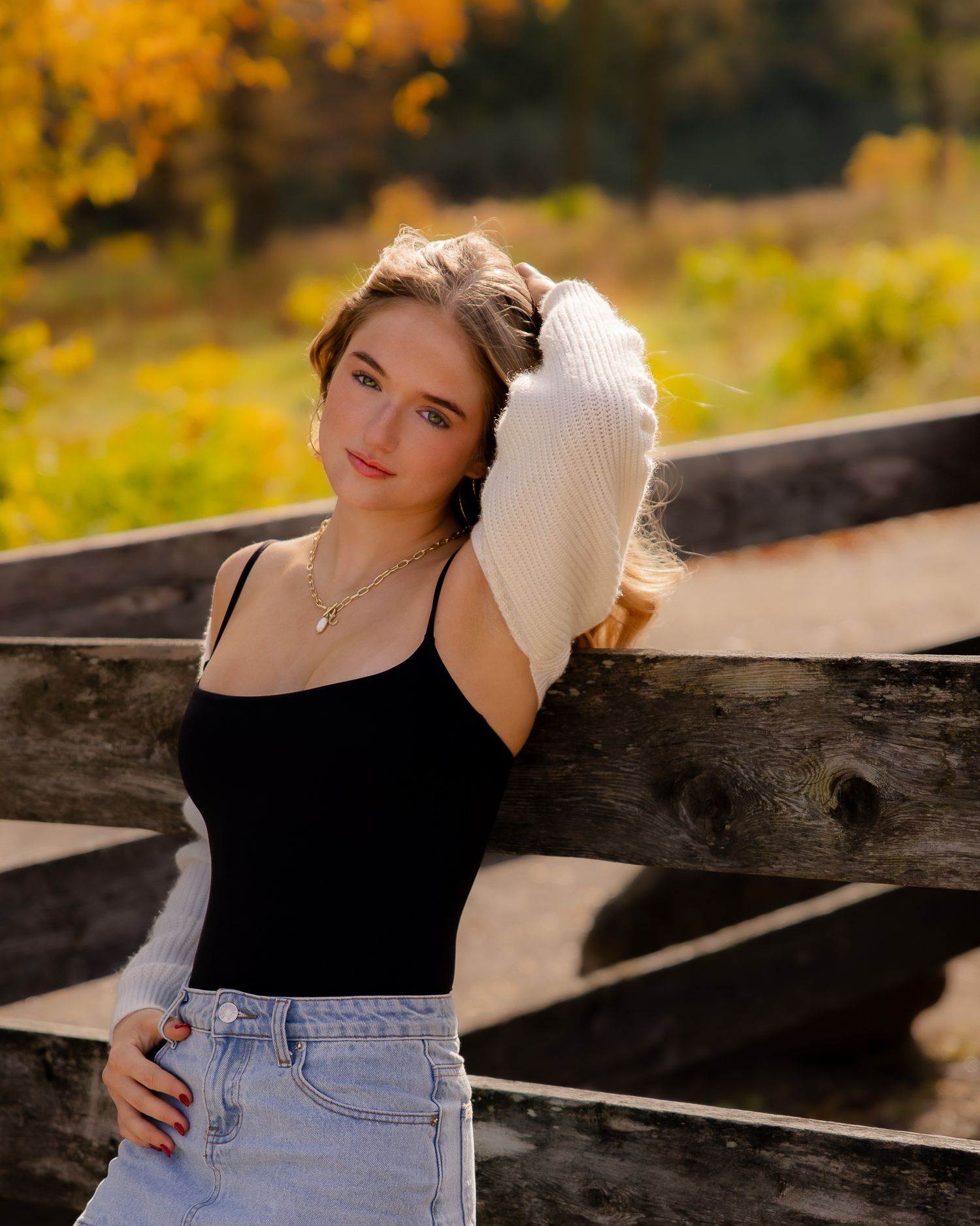 A casual portrait session featuring someone wearing a black top and denim against an autumn background.