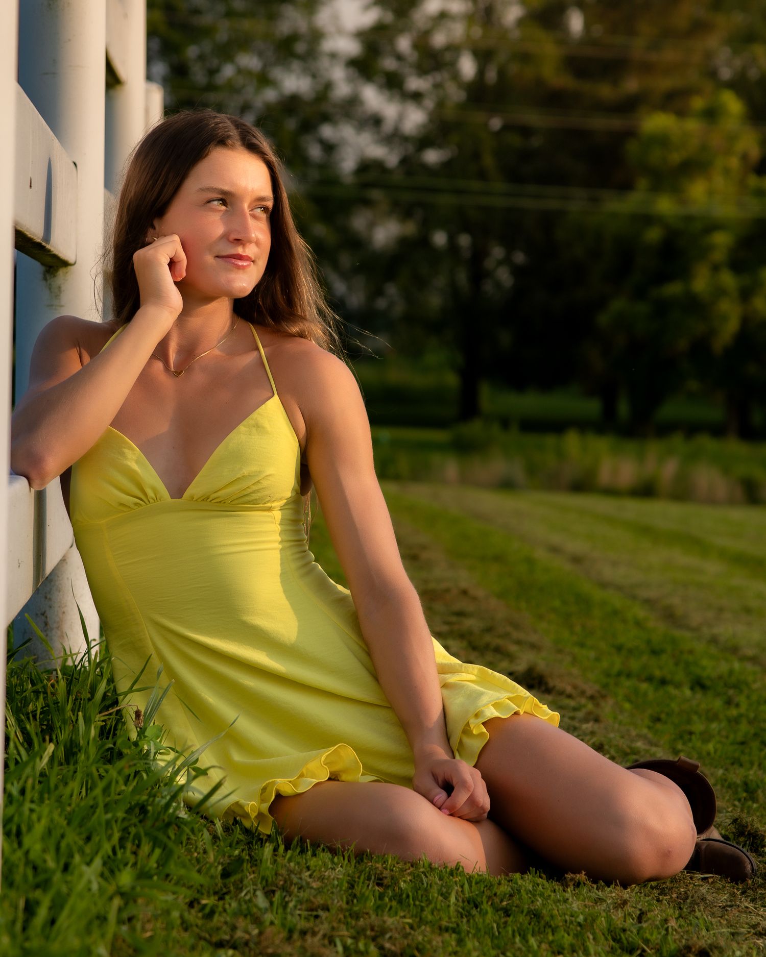 A person in a bright yellow dress lounges gracefully in the grass at sunset, creating a warm summer aesthetic.