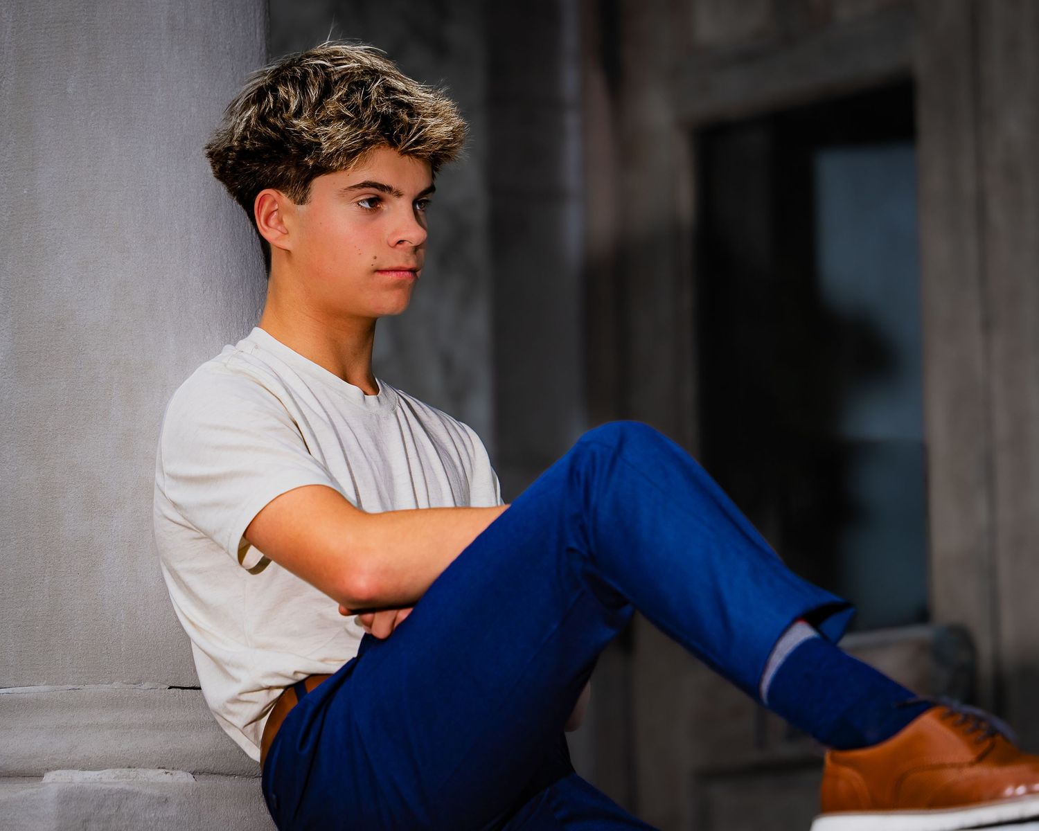 Person in white t-shirt and blue pants sitting on concrete ledge during outdoor photoshoot.