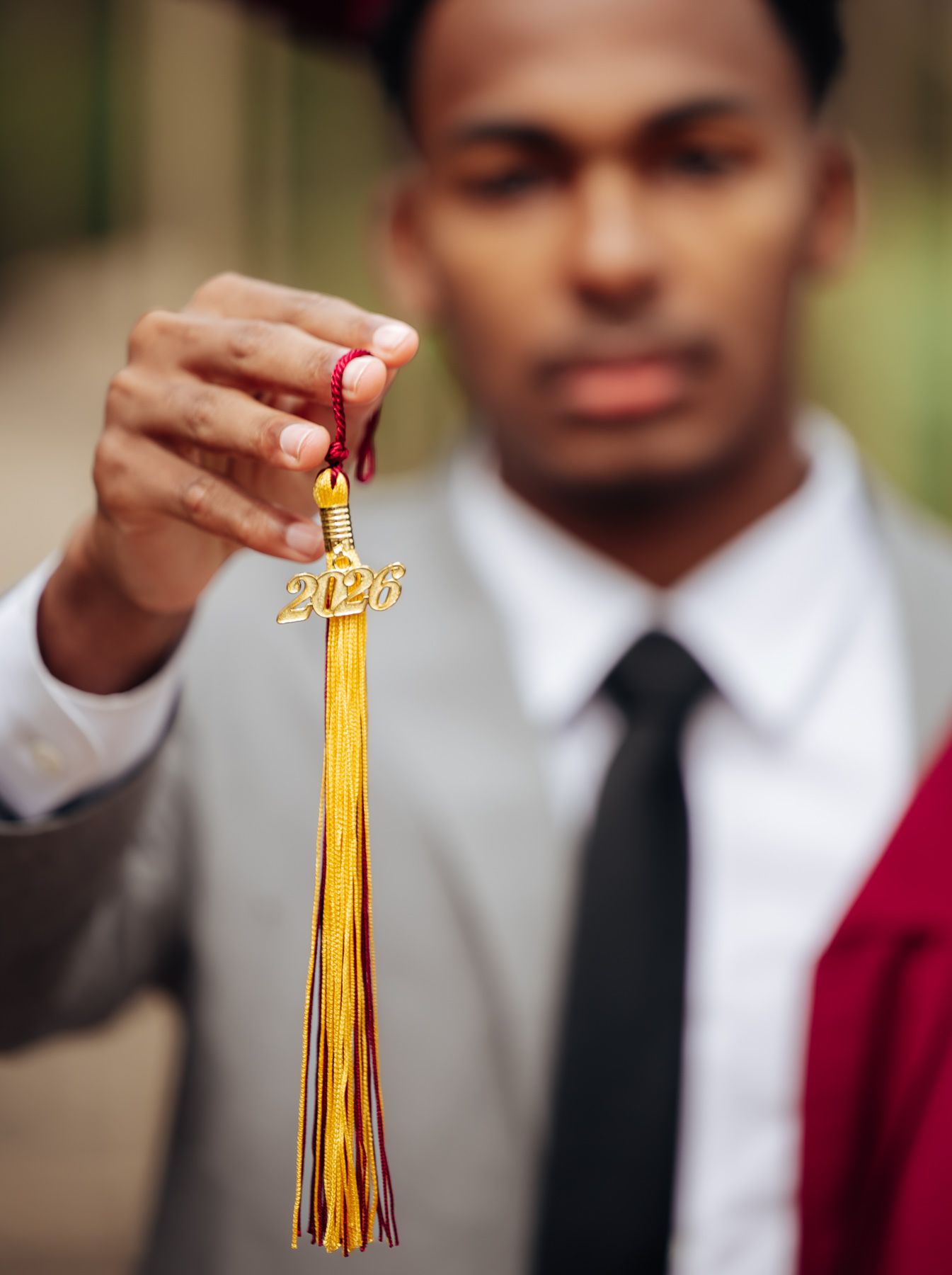 A young man in a suit holds up a gold 2025 graduation tassel, symbolizing academic achievement.