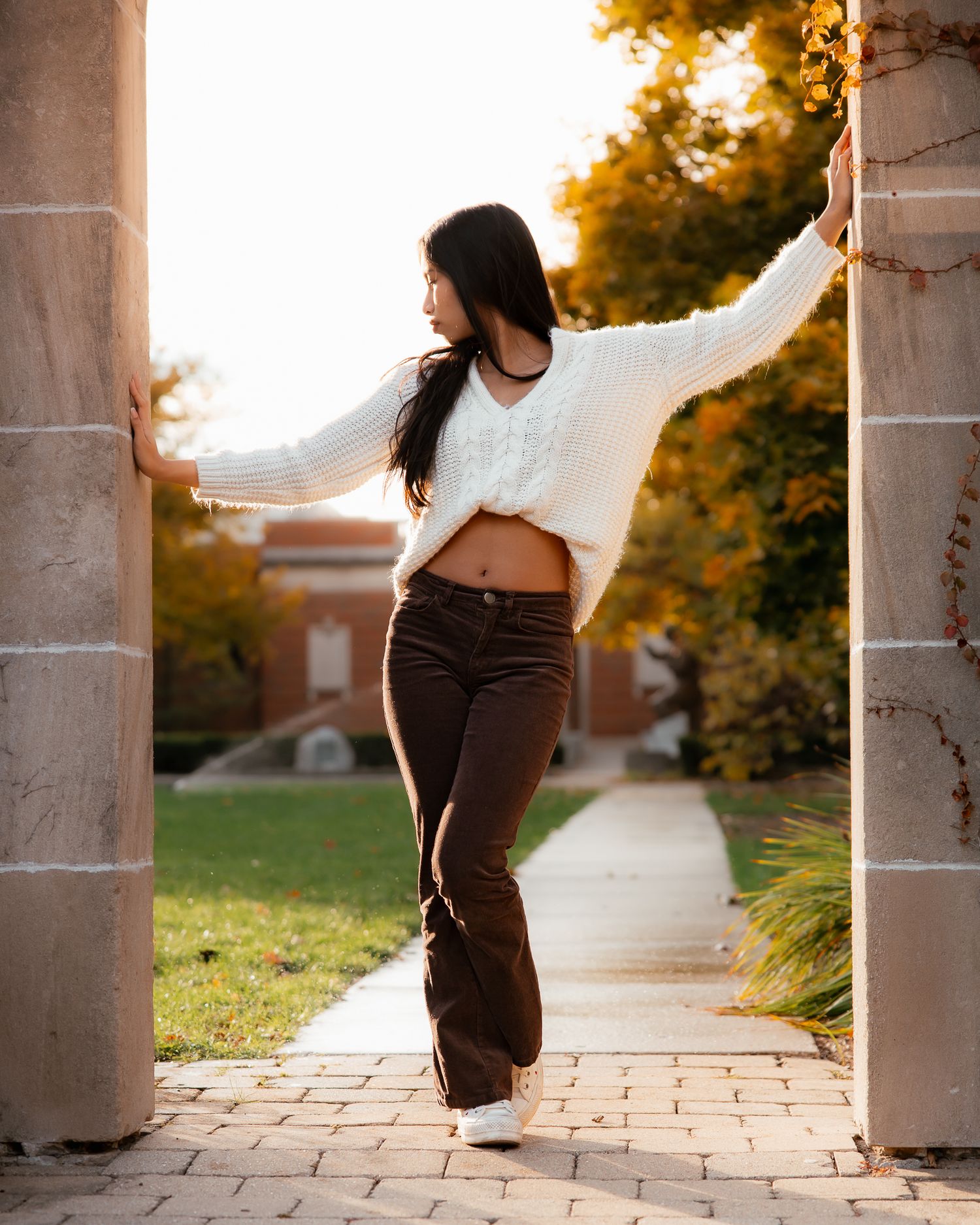 A figure in brown pants and white top dances gracefully between stone pillars at sunset.