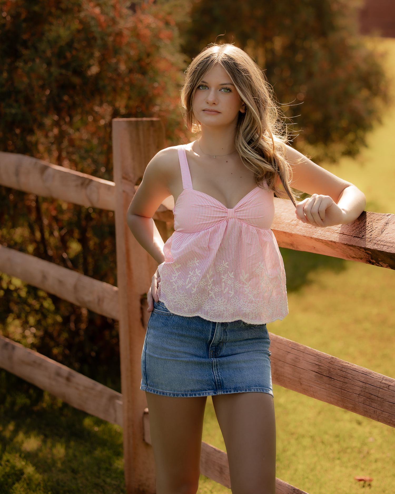 Summer fashion portrait by rustic wooden fence featuring pink top and denim skirt.