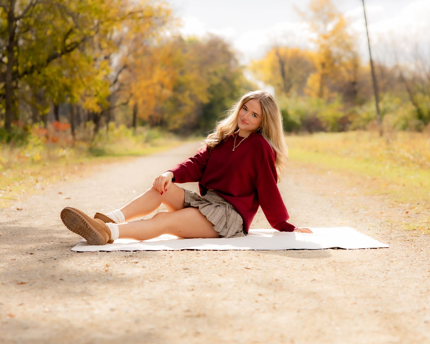 Cozy fall photoshoot on a blanket along a nature path with autumn foliage.