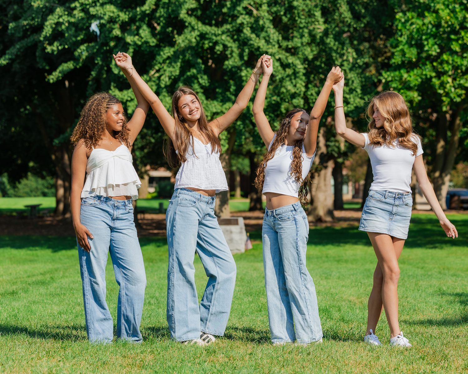 Group in matching white tops and blue jeans posing playfully on green grass in a park setting.