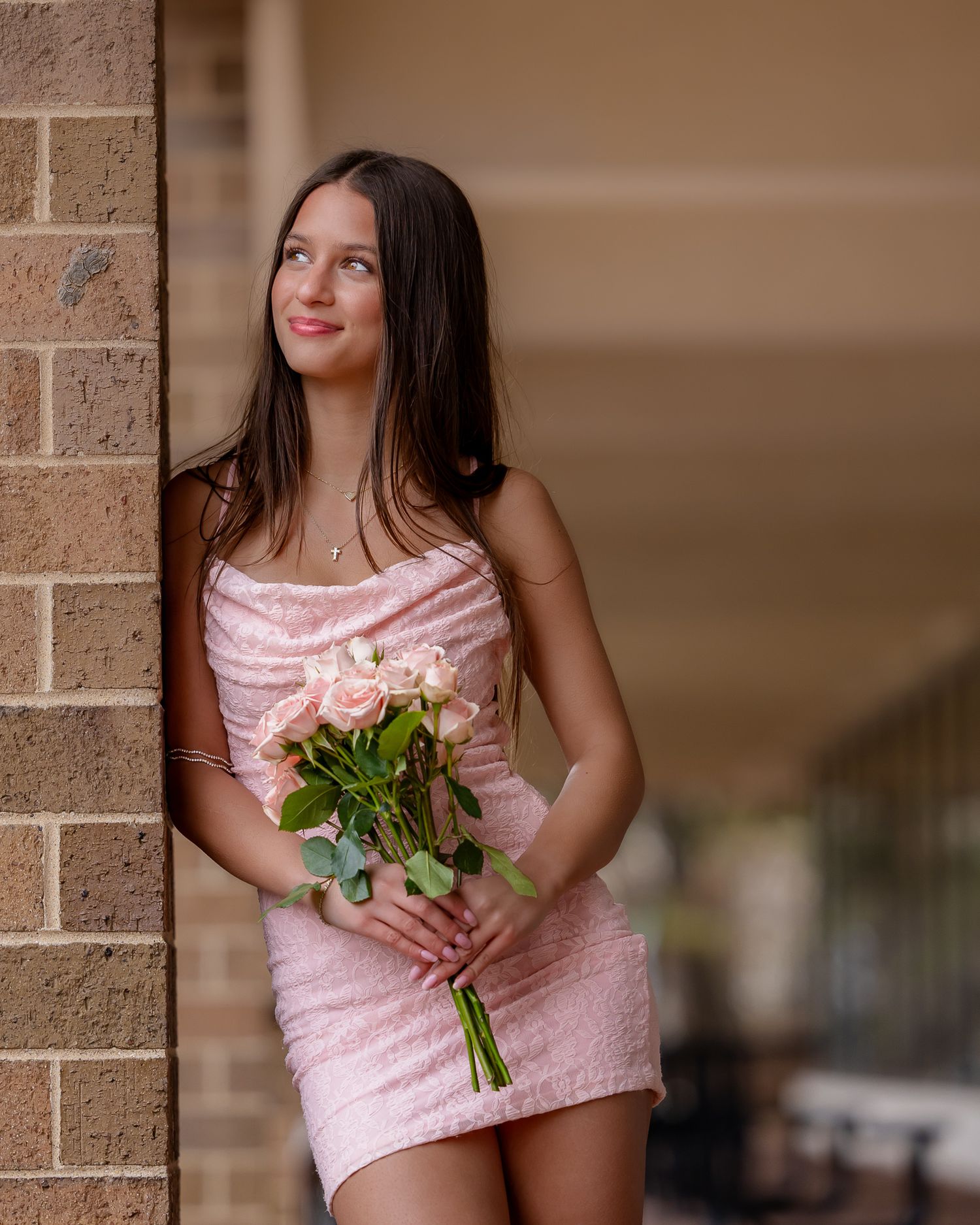 A person in a pink striped top poses against a brick wall while holding a bouquet of white roses.