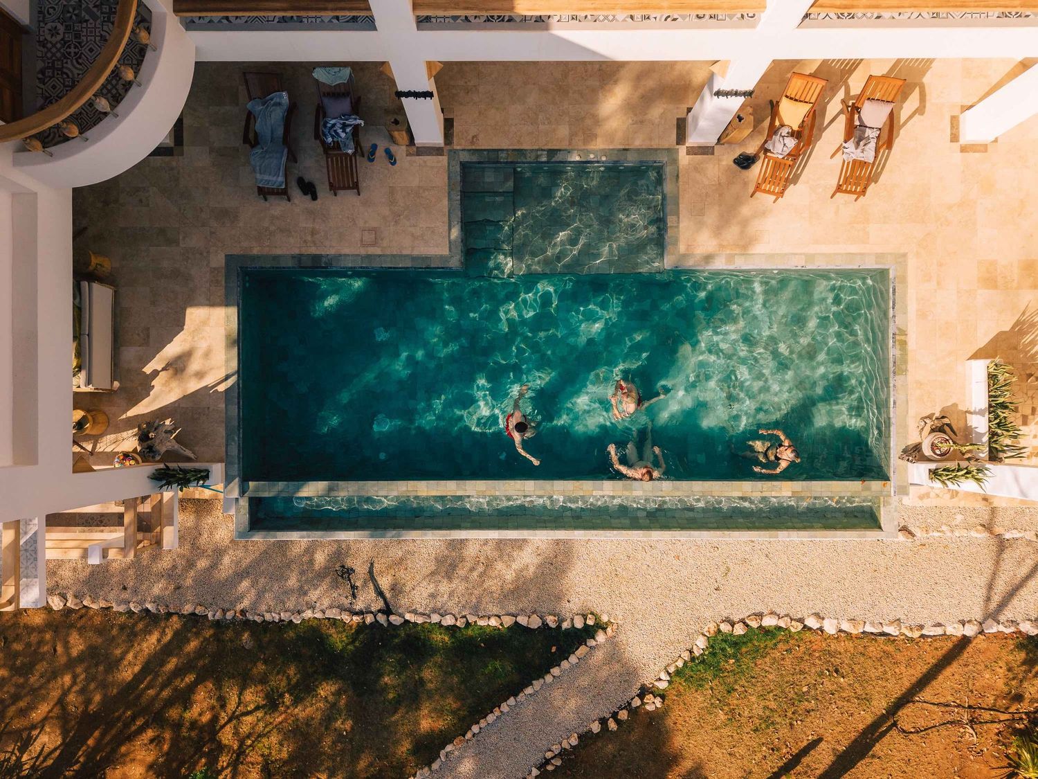 Aerial view of swimmers in a turquoise rectangular pool surrounded by lounge chairs and stone paving.