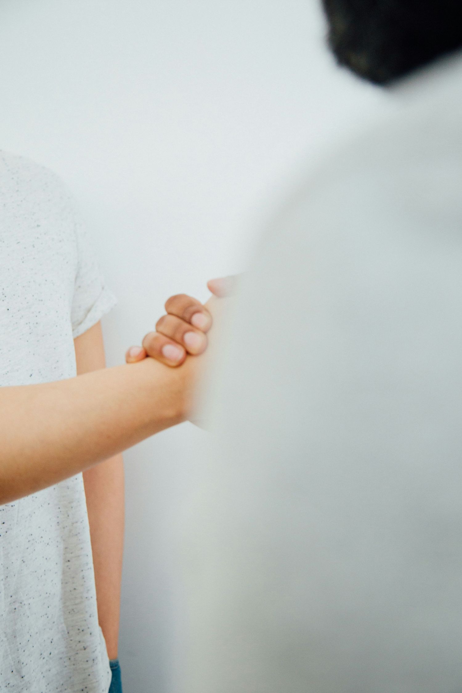 Close-up of couple holding hands tenderly against a soft white background in casual clothing.