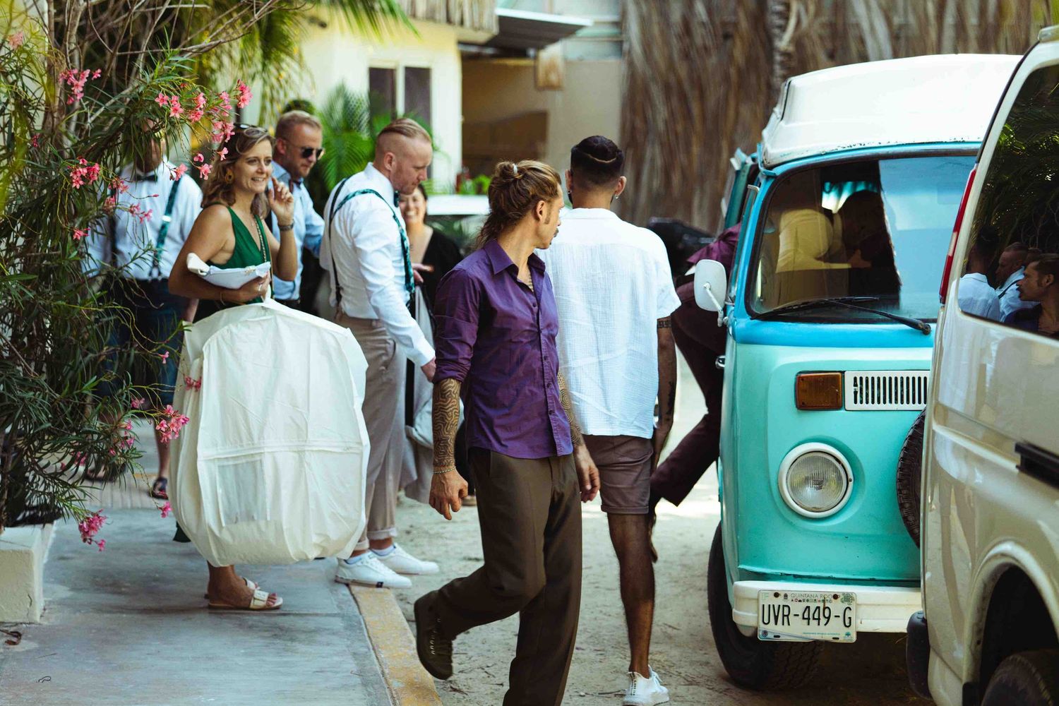 Wedding party gathering near a vintage turquoise van on a sunny street before the ceremony.
