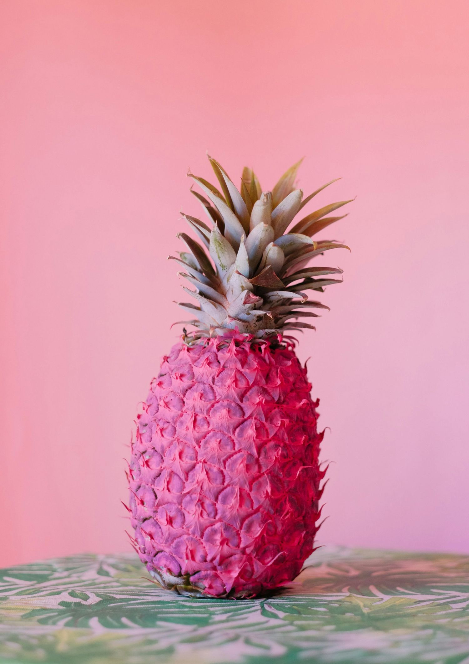 Vibrant pink painted pineapple on colorful surface against bright pink background.
