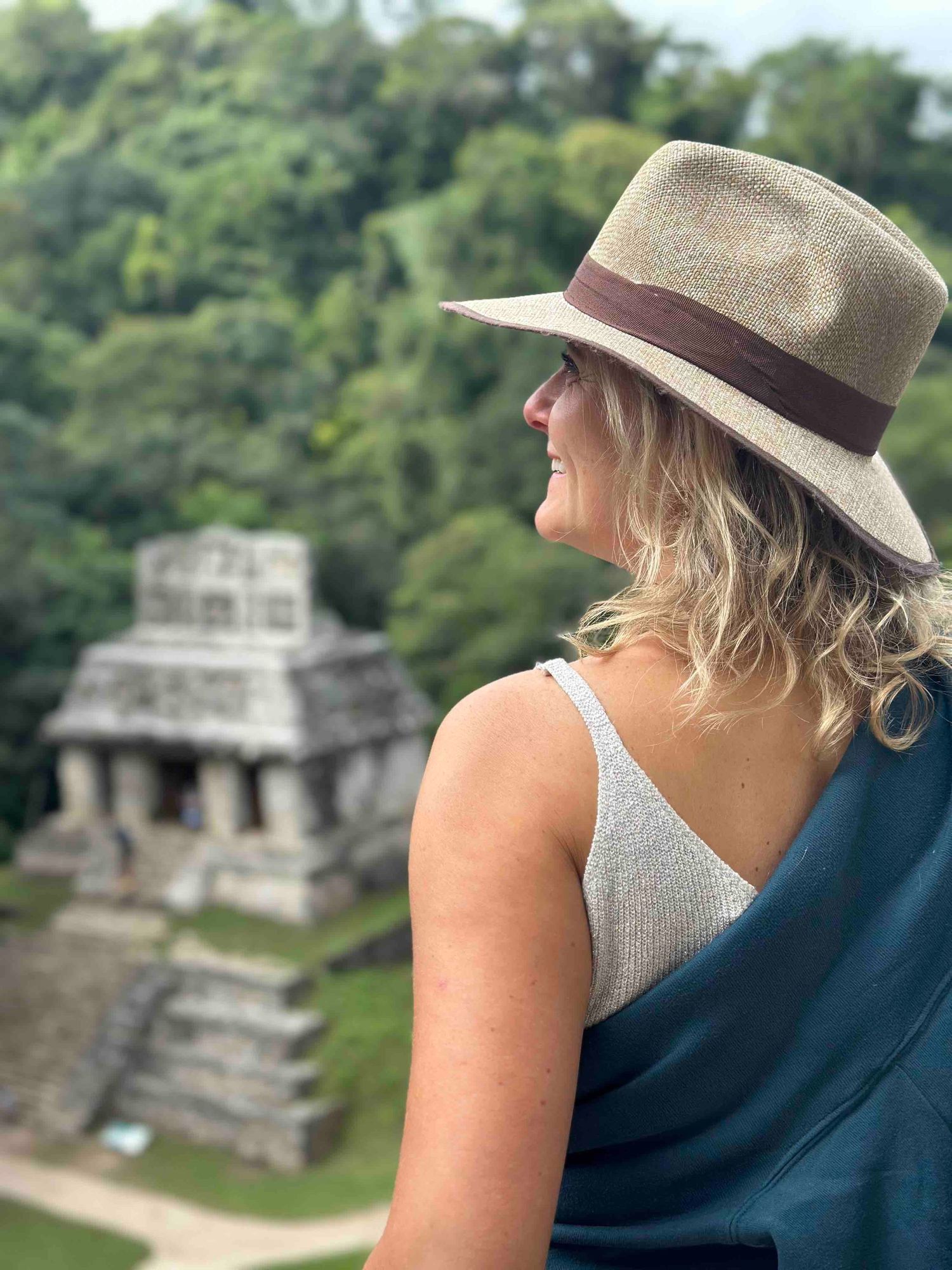 Woman in a hat gazing at ancient Mayan ruins surrounded by lush tropical jungle.