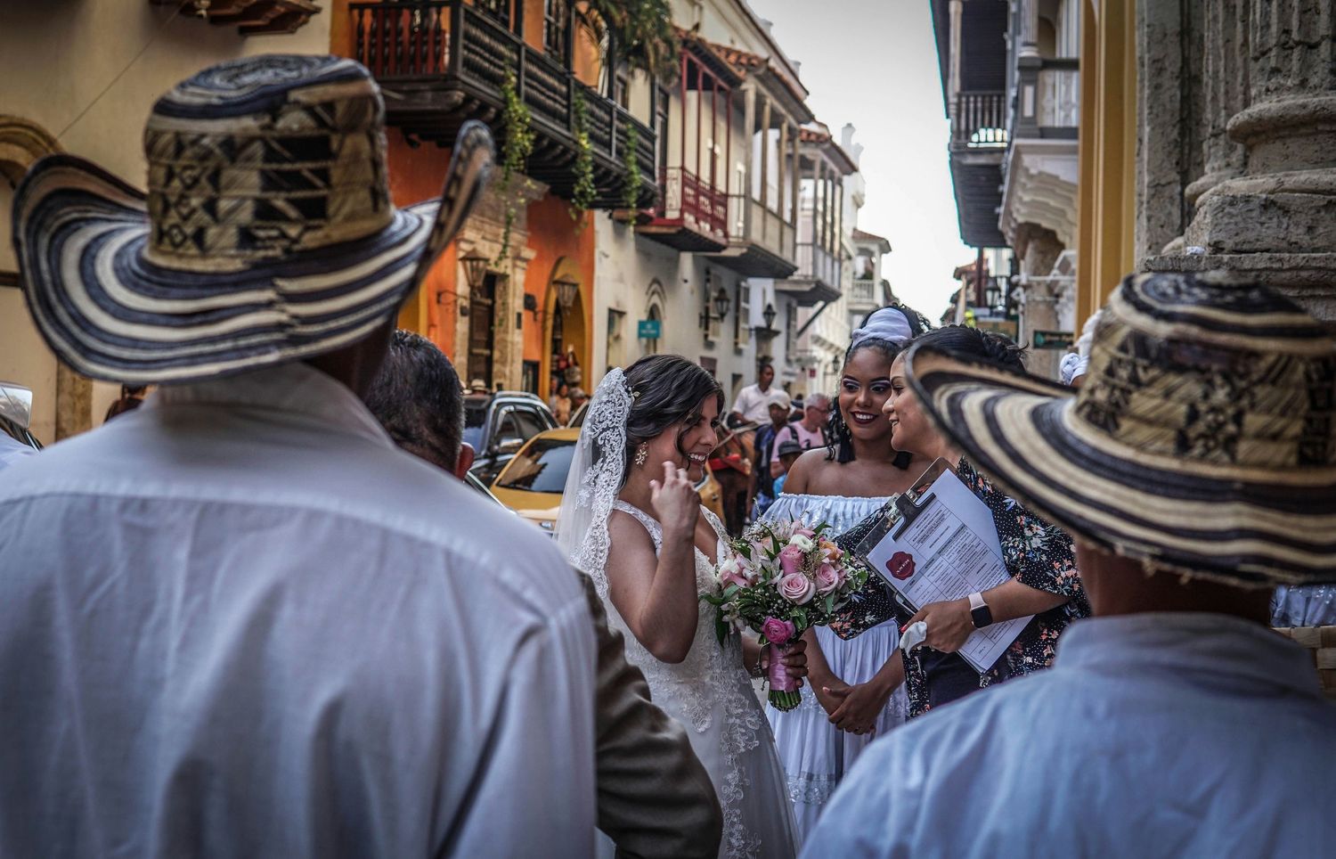 Wedding couple surrounded by guests wearing traditional Colombian sombrero vueltiao hats on a colorful street.