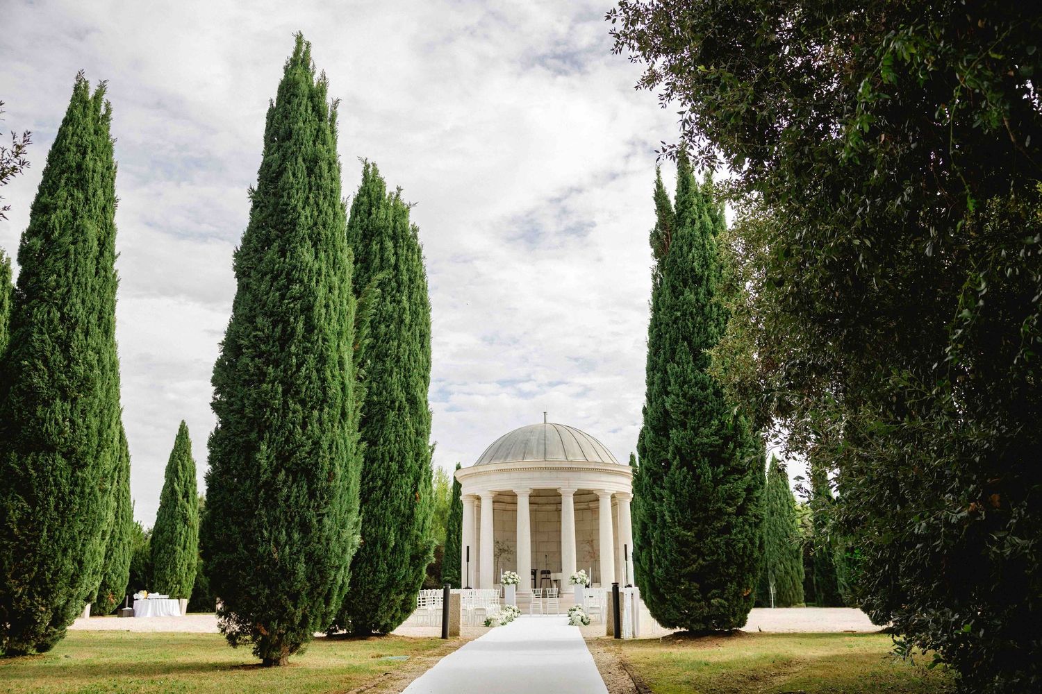 Elegant neoclassical domed wedding venue framed by tall Italian cypress trees along a manicured pathway.