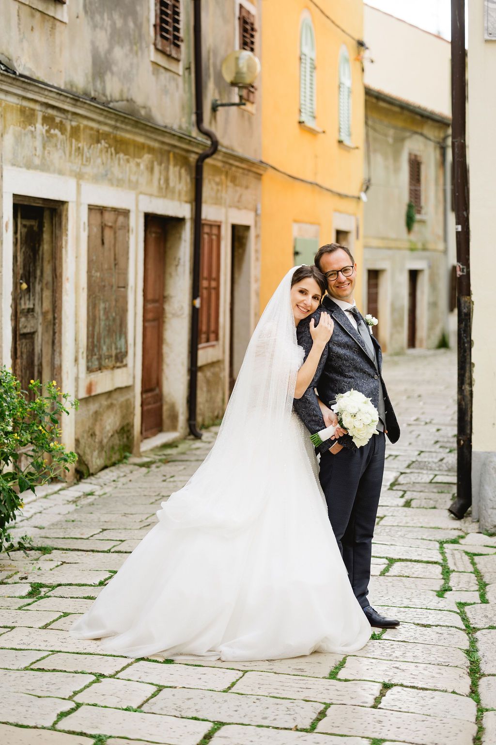 Bride and groom posing on a cobblestone street with colorful old European buildings in the background.
