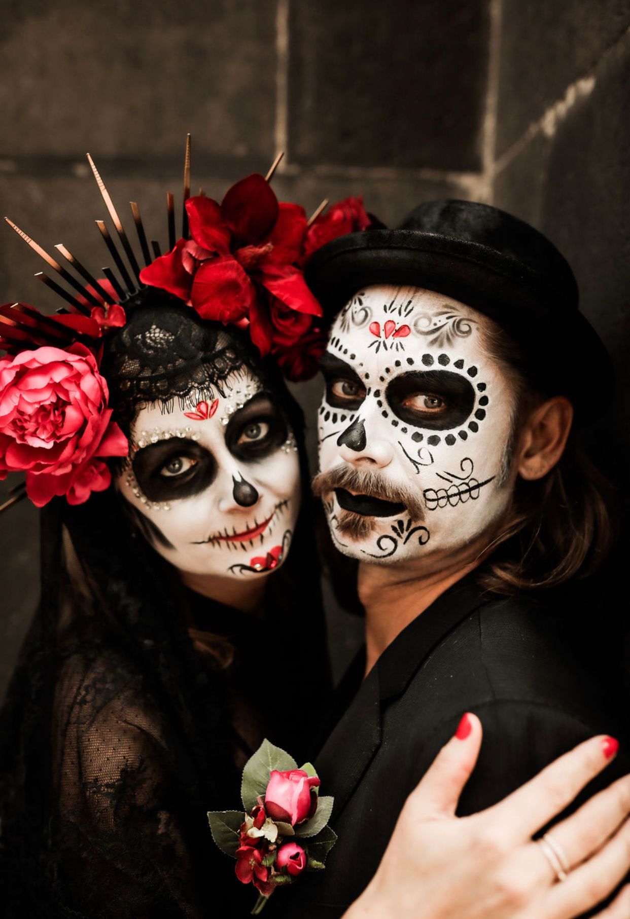 Couple wearing elaborate Day of the Dead sugar skull face paint and floral headpiece for Halloween.
