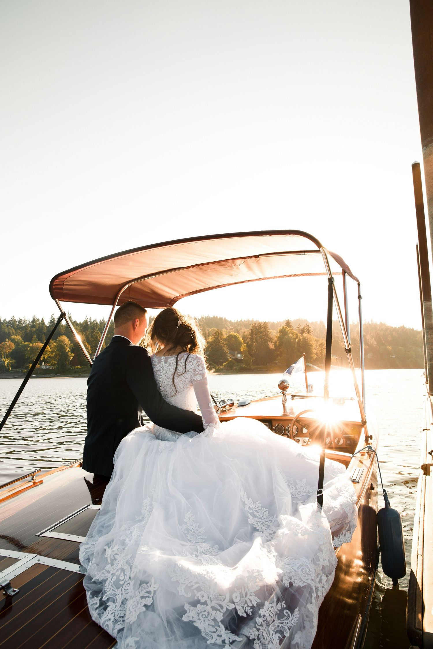 Newlyweds sitting together on wooden boat deck bathed in golden sunset light.