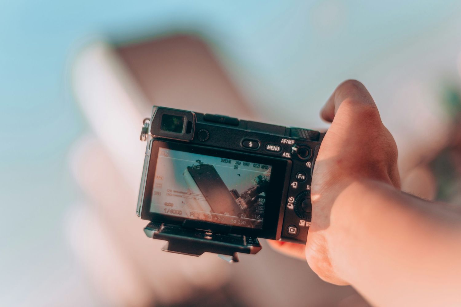 Hands holding digital camera photographing beach scene in bright natural sunlight.