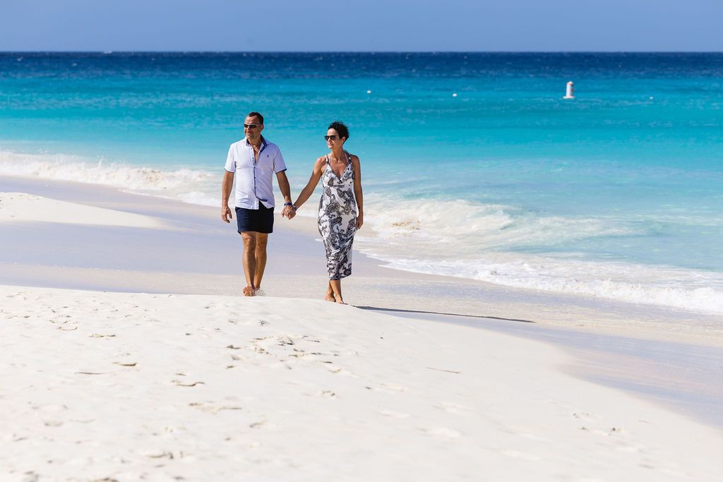 A couple walks hand-in-hand along a pristine white sandy beach with turquoise water.