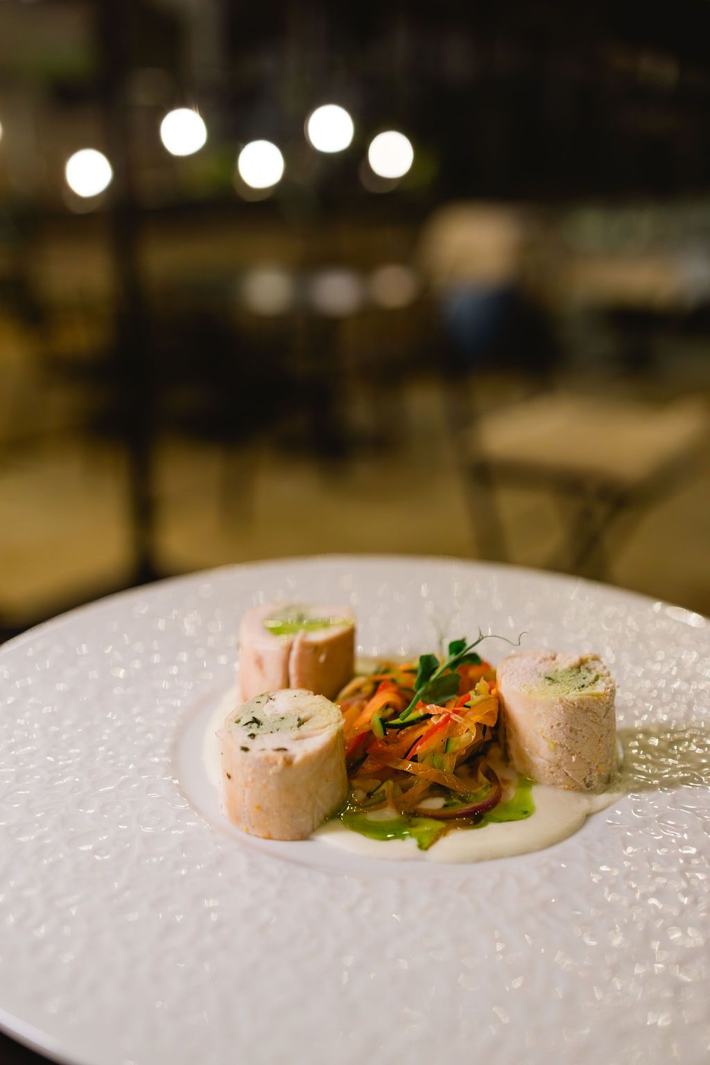 Gourmet stuffed meat rolls with pickled vegetables and herb sauce on white plate at upscale restaurant.