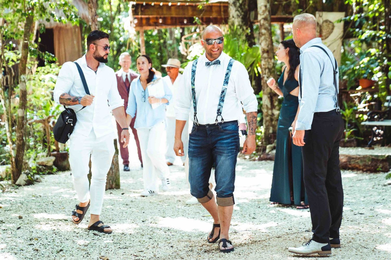 Wedding guests in casual attire walking along a gravel path in a tropical outdoor venue.