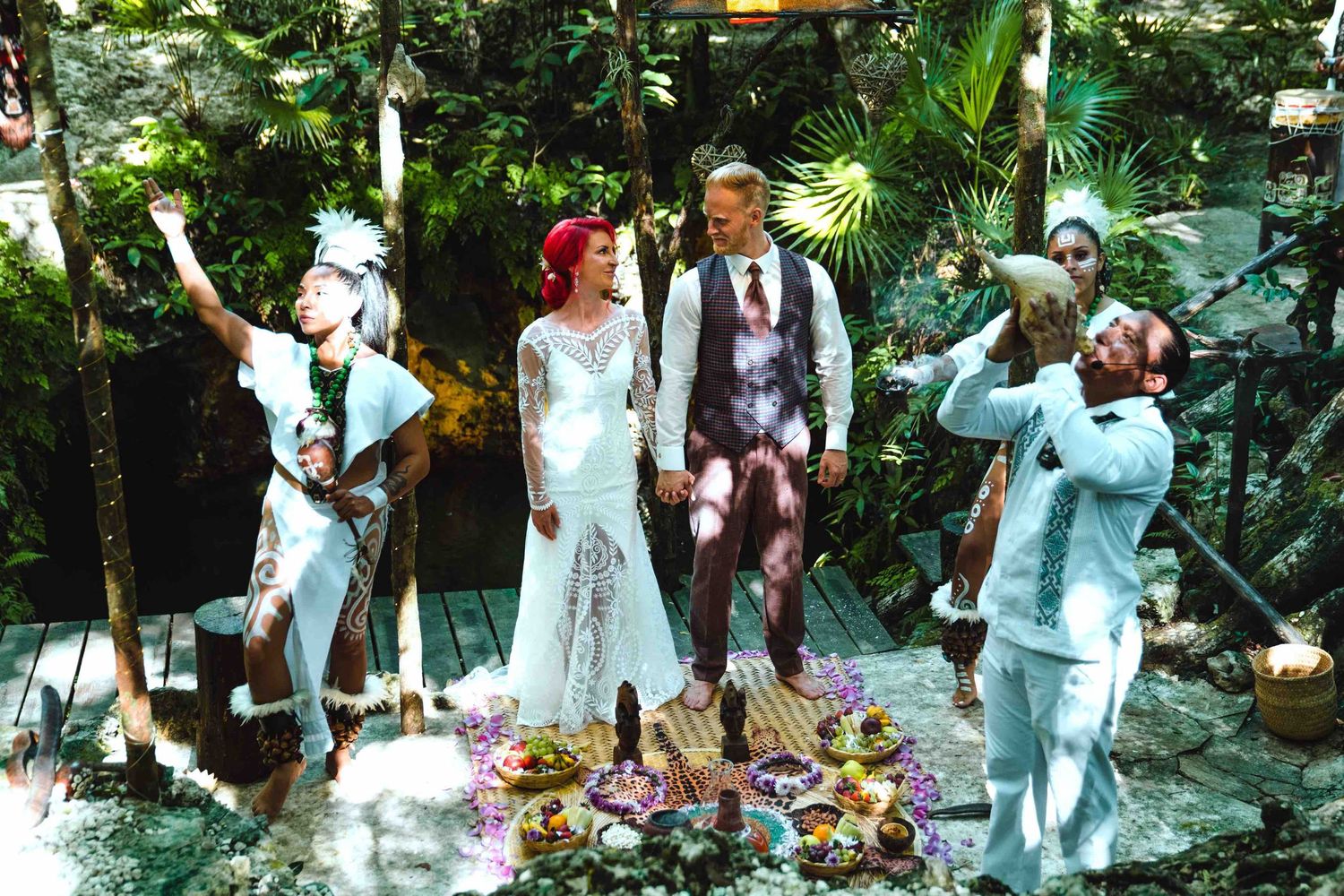Bride and groom standing with ceremonial performers during a colorful Mayan jungle wedding ritual.