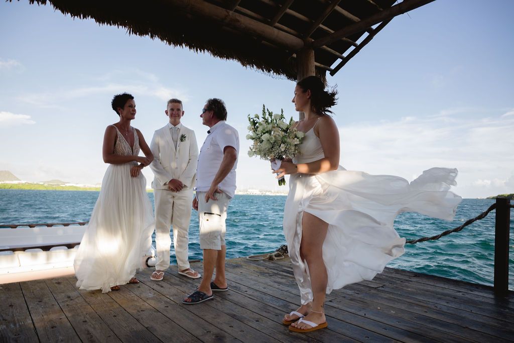 Beach wedding ceremony on a wooden dock overlooking turquoise ocean waters.
