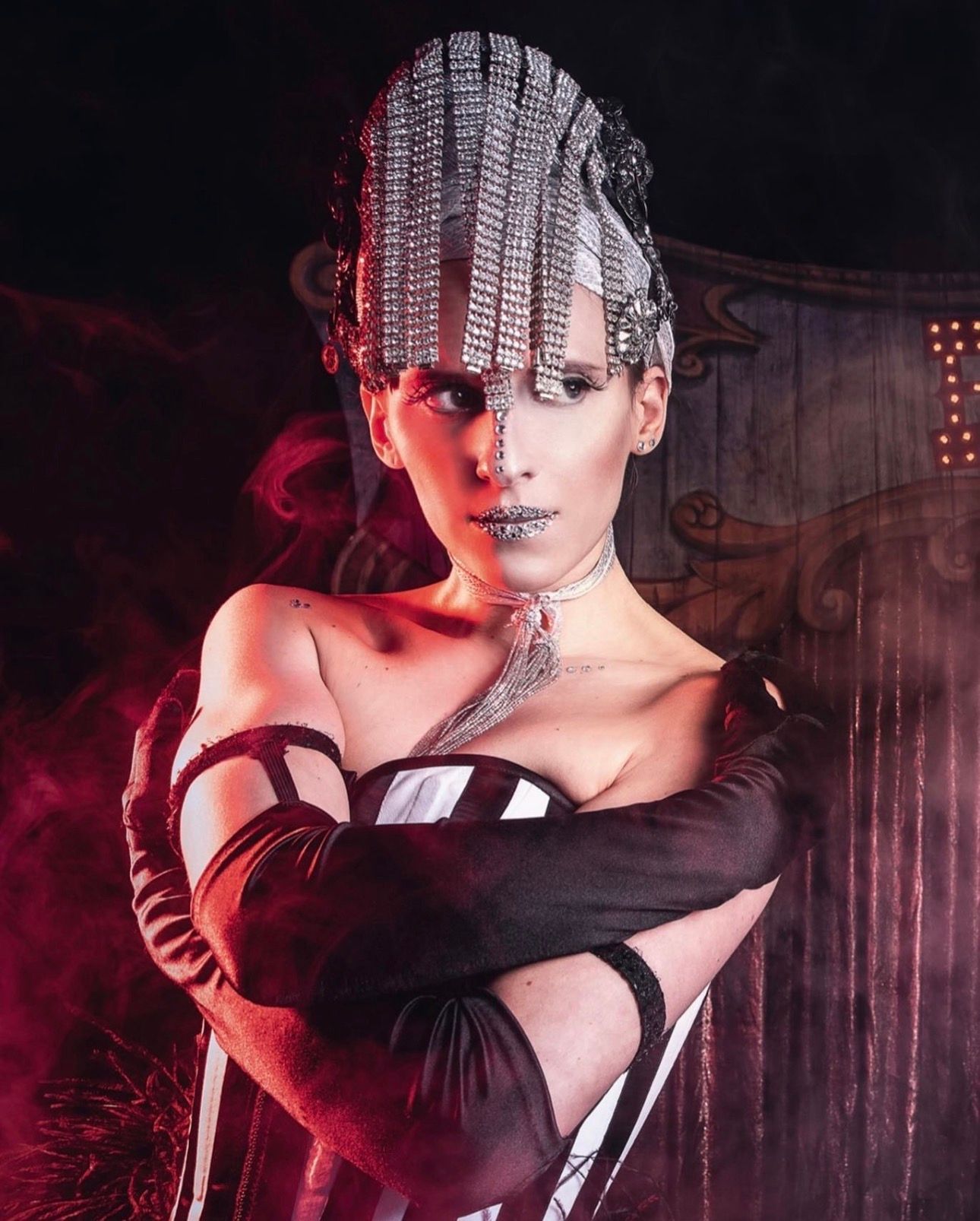 Dramatic portrait of a woman in avant-garde silver headdress and black costume against dark red backdrop.