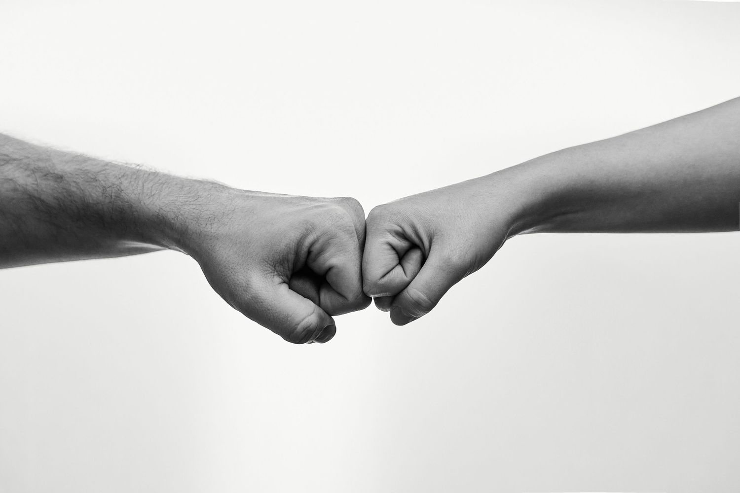 Two fists bumping together in a black and white close-up photo symbolizing teamwork and unity.
