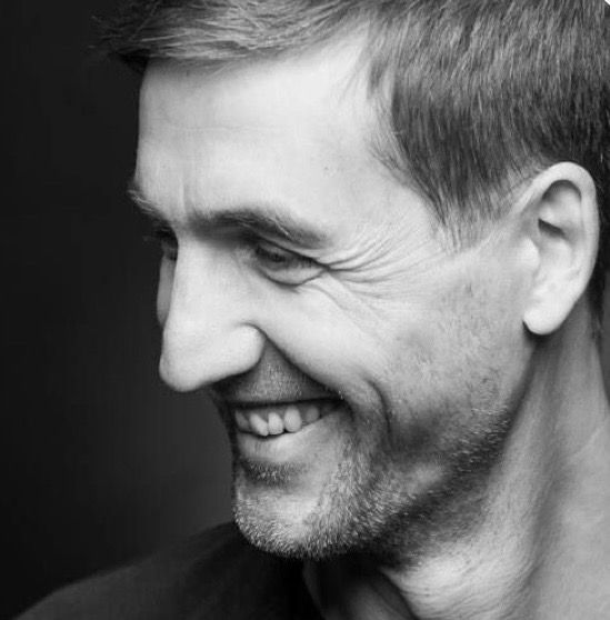 Close-up black and white profile portrait of a smiling man with short hair and stubble.