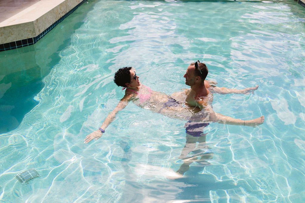 Two people swimming and relaxing together in a bright turquoise outdoor pool.