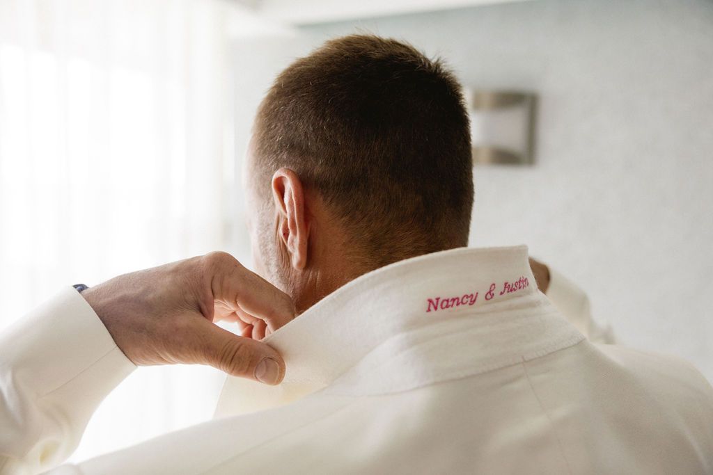 Close-up of groom's white shirt collar with embroidered names Nancy and Justin in red.