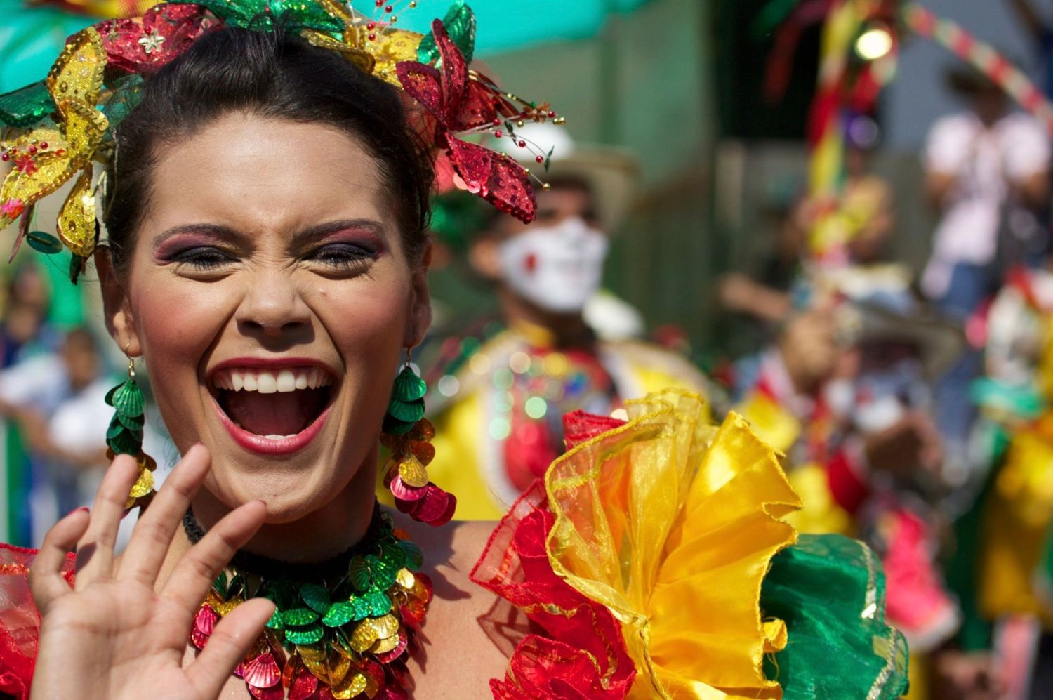 Joyful woman in vibrant colorful carnival costume laughing at a festive street parade celebration.