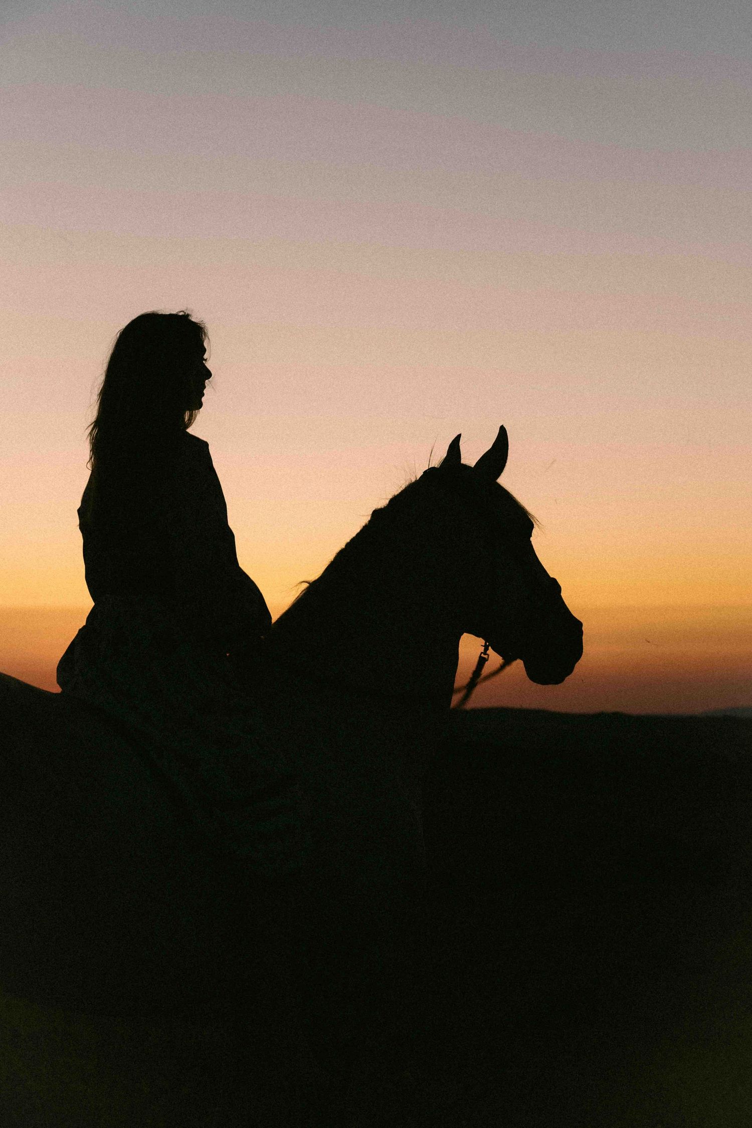 Silhouette of a woman riding a horse against a vibrant orange and purple sunset sky.