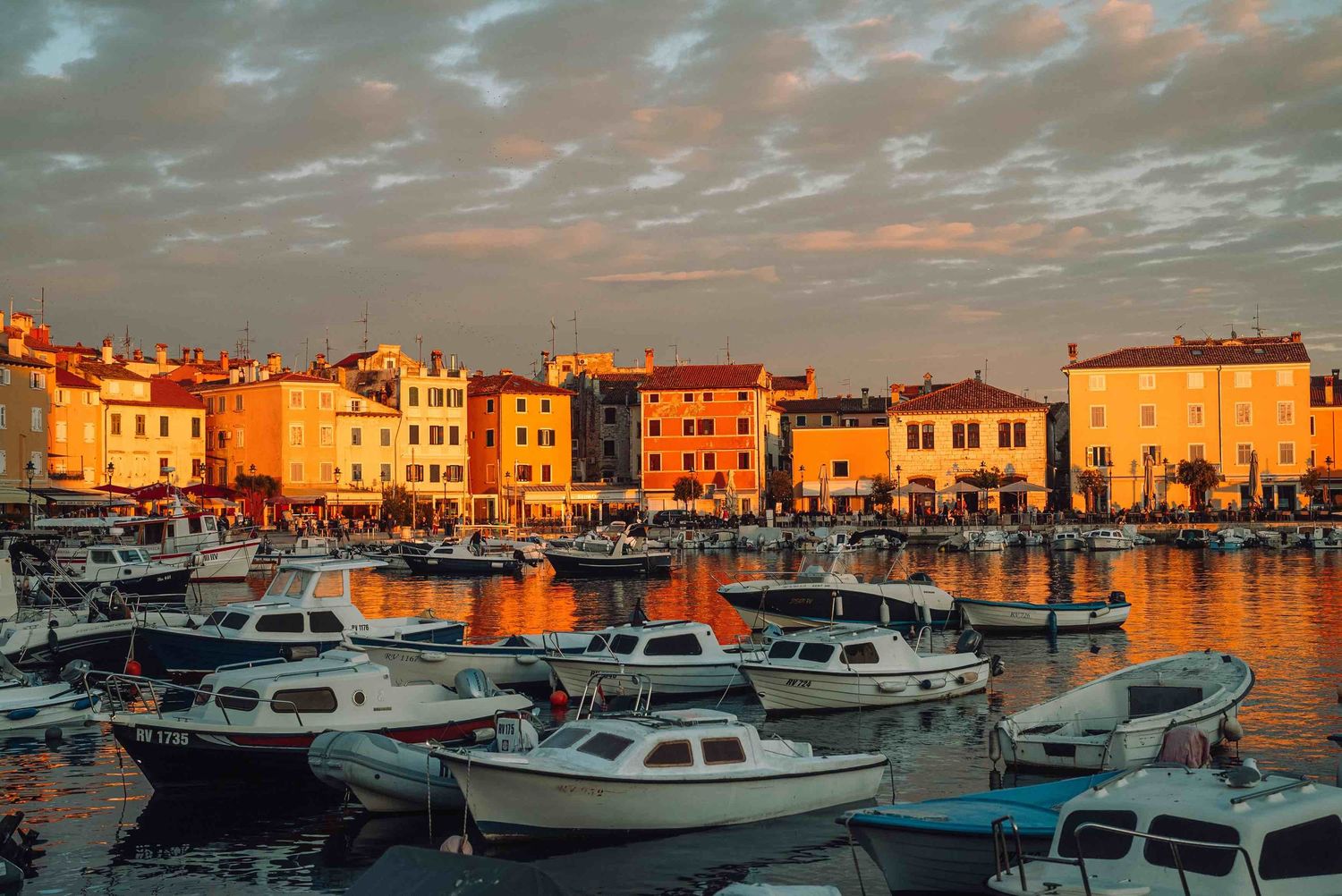 Colorful waterfront buildings reflecting golden sunset light over a marina filled with boats in Rovinj, Croatia.