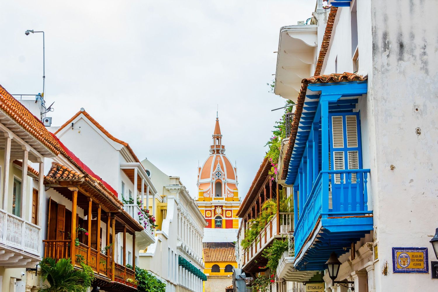 Charming colonial street in Cartagena Colombia with colorful balconies and cathedral tower backdrop.
