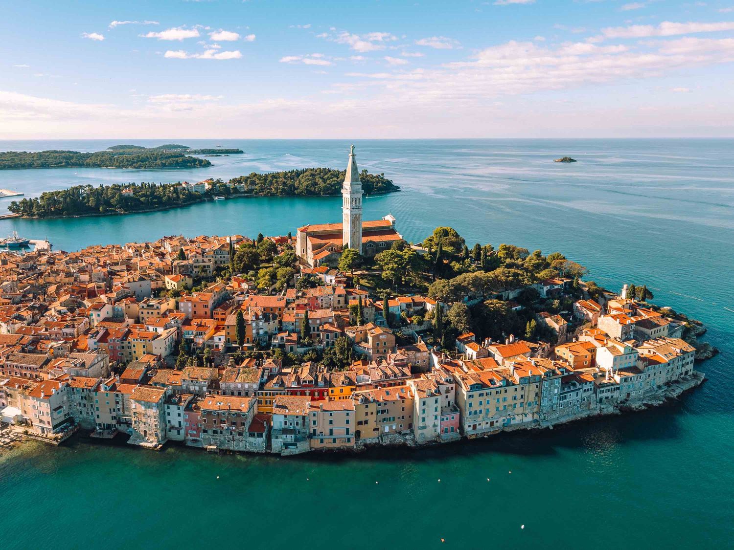 Aerial view of Rovinj, Croatia, a historic coastal town on a peninsula with orange rooftops and a church tower.