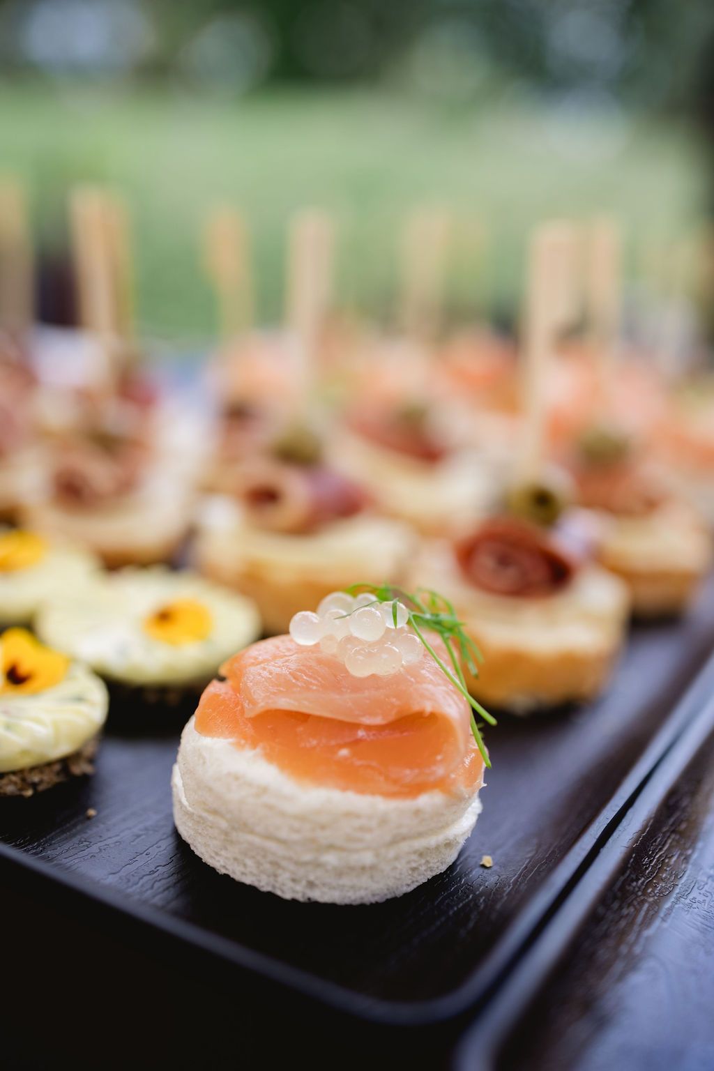 Elegant smoked salmon canape with caviar and cream cheese on a dark serving tray at a wedding reception.