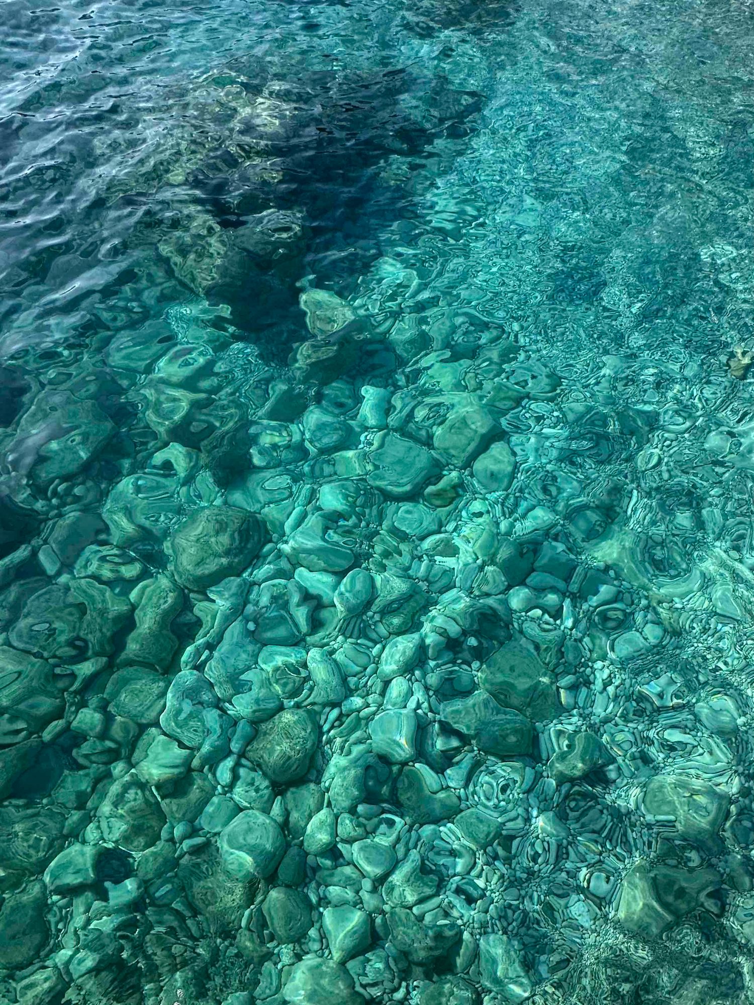 Crystal clear turquoise water revealing colorful smooth stones on a rocky Mediterranean seabed.