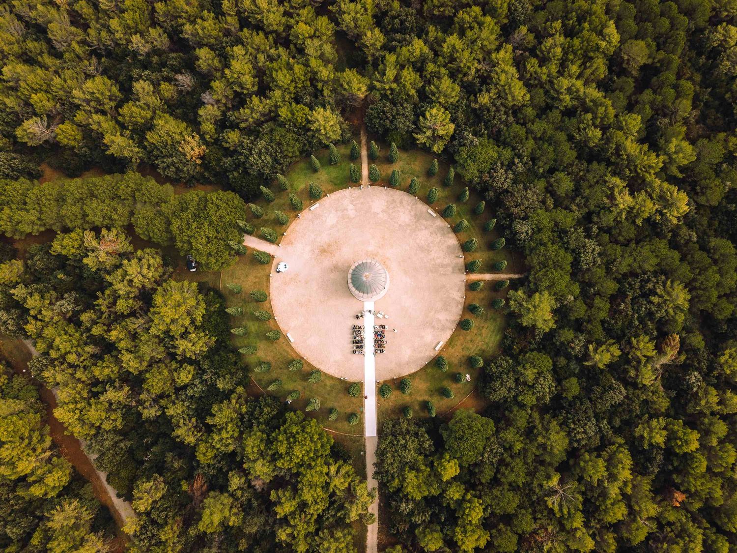 Aerial drone view of a circular platform tower surrounded by lush green forest trees from above.