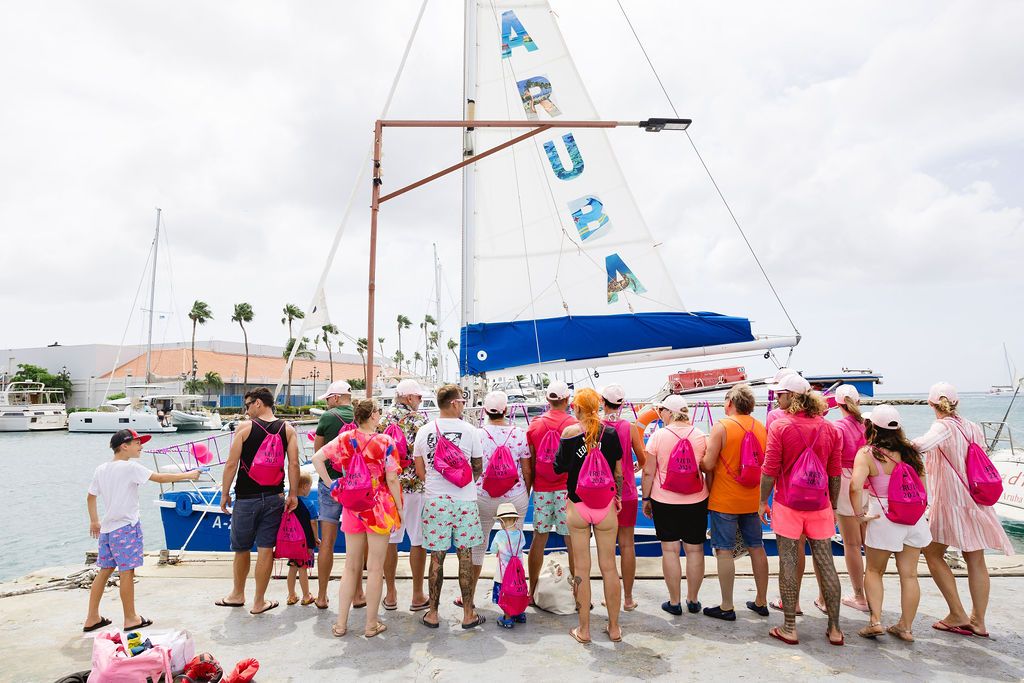 Group of women in pink outfits boarding an Aruba sailboat at a sunny harbor.
