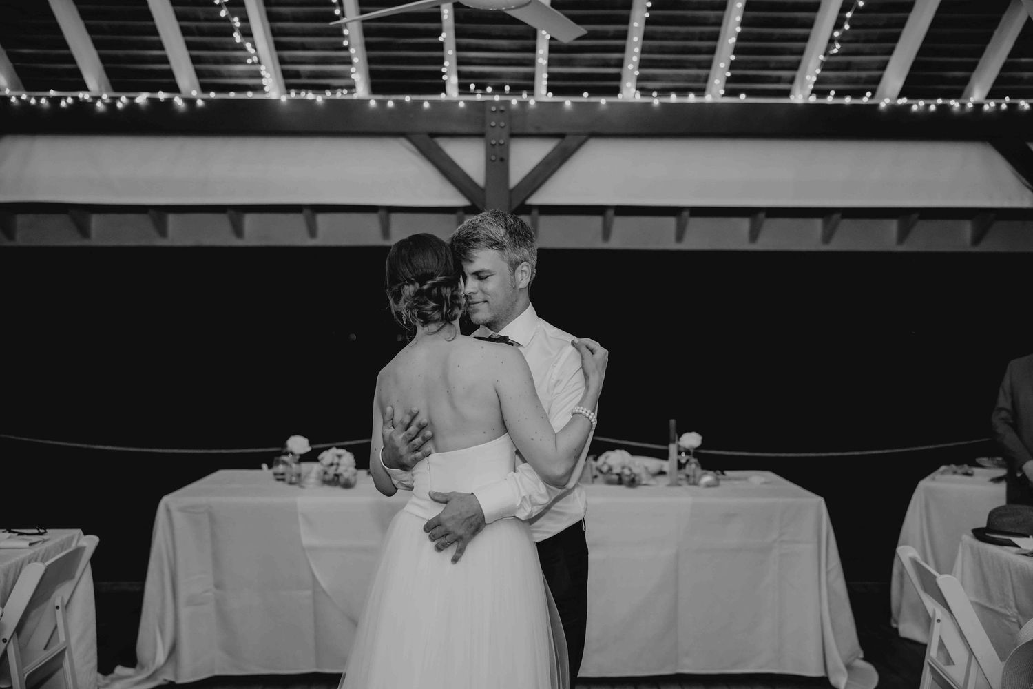 Bride and groom share an intimate first dance in black and white at a softly lit reception venue.