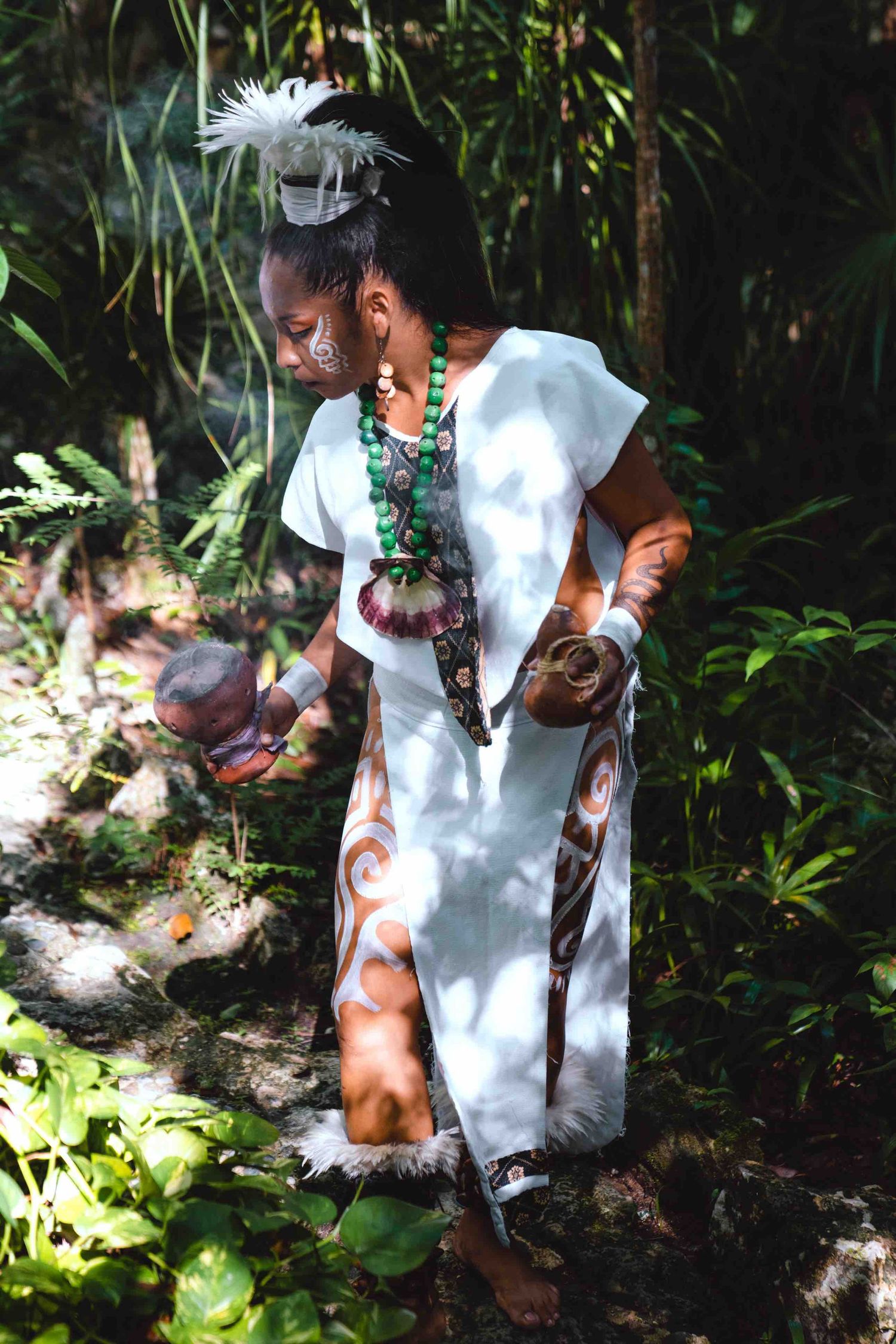 Mayan shaman in traditional white ceremonial dress with beaded necklace performing a ritual in jungle.