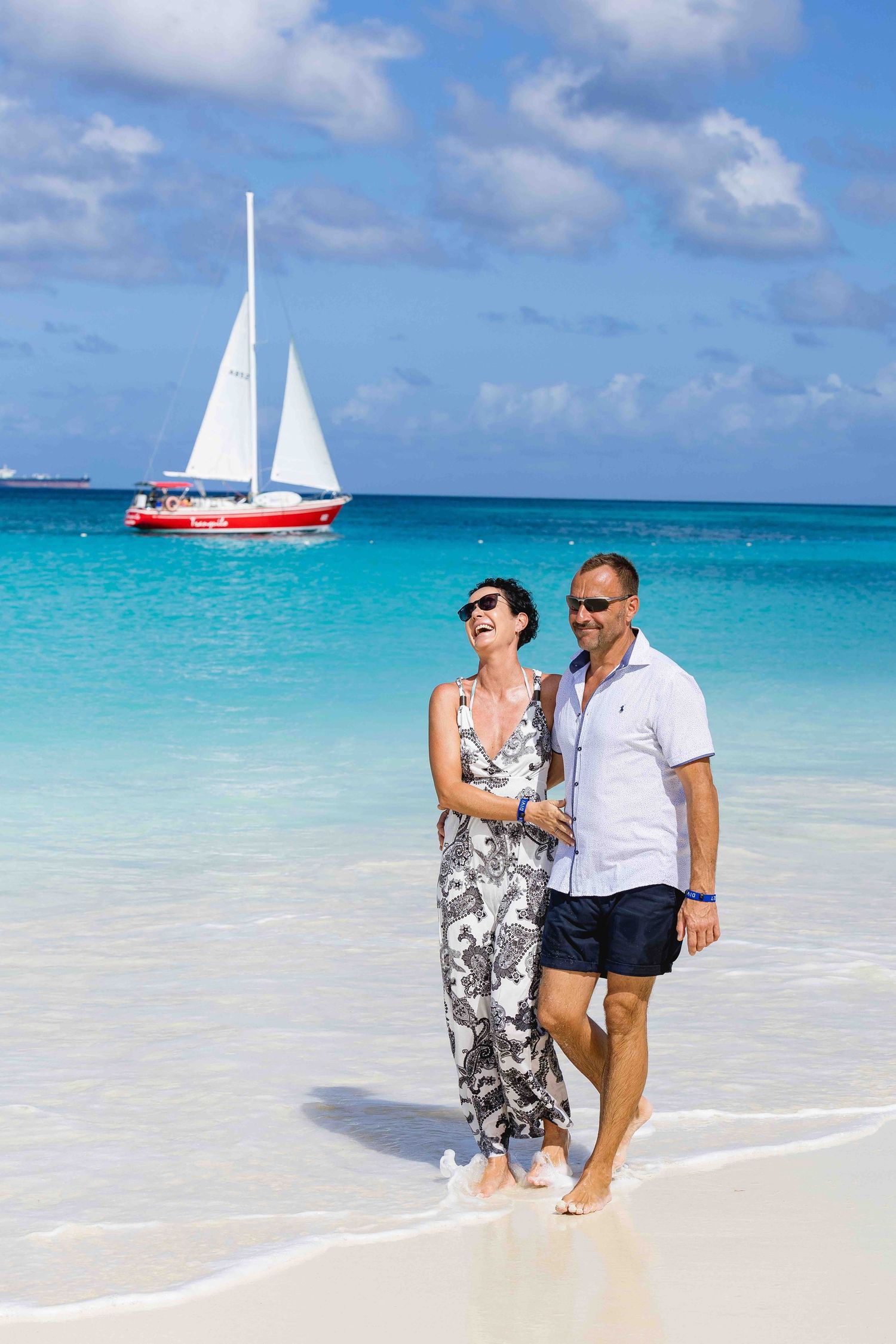 Romantic couple walking barefoot on a tropical beach with clear turquoise ocean water.
