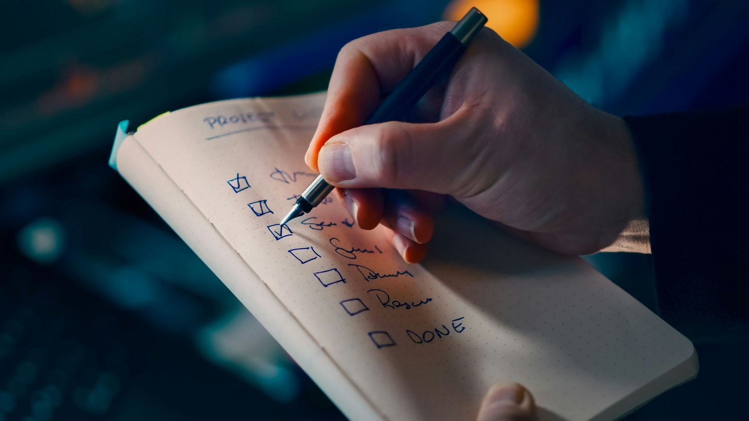 Close-up of hand writing checklist in notebook with pen under warm lighting.