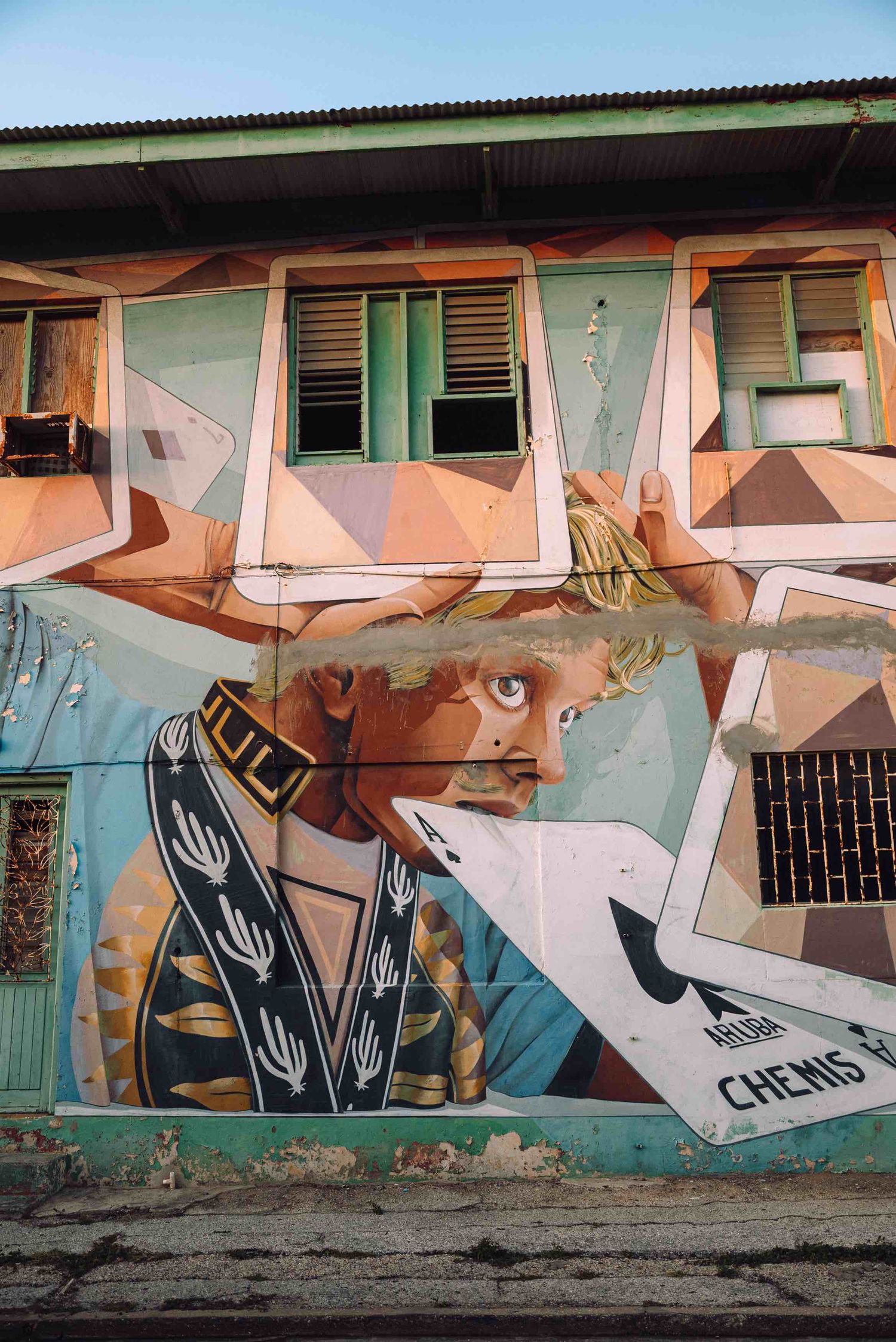 Colorful street art mural on a building wall featuring a blonde figure holding playing cards with urban graffiti elements.