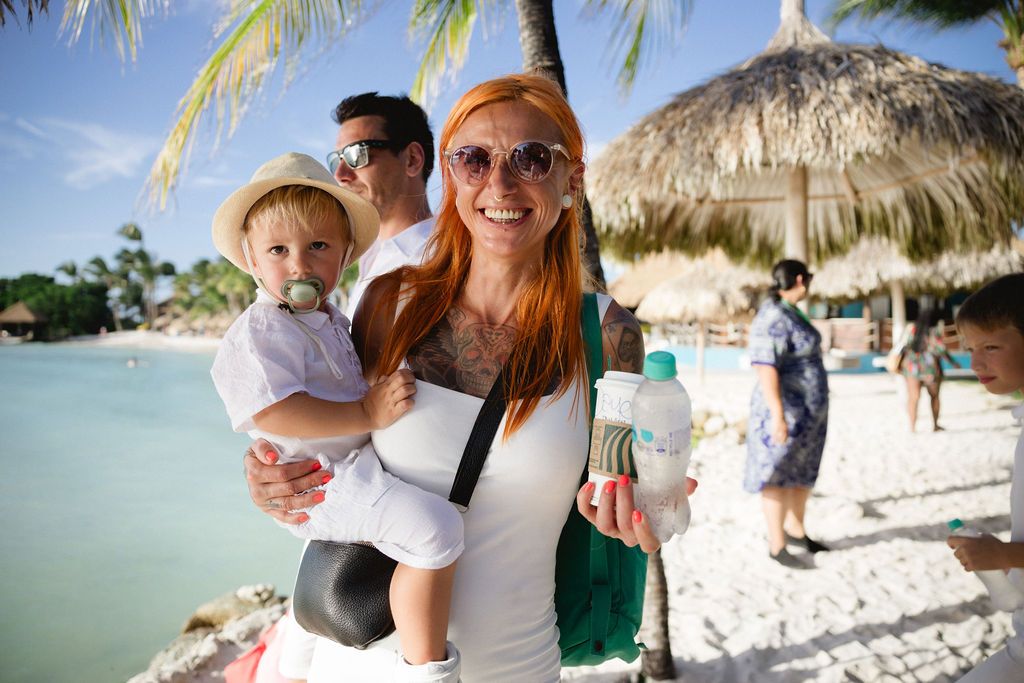 Smiling redhead woman holding a toddler on a sunny tropical beach resort.