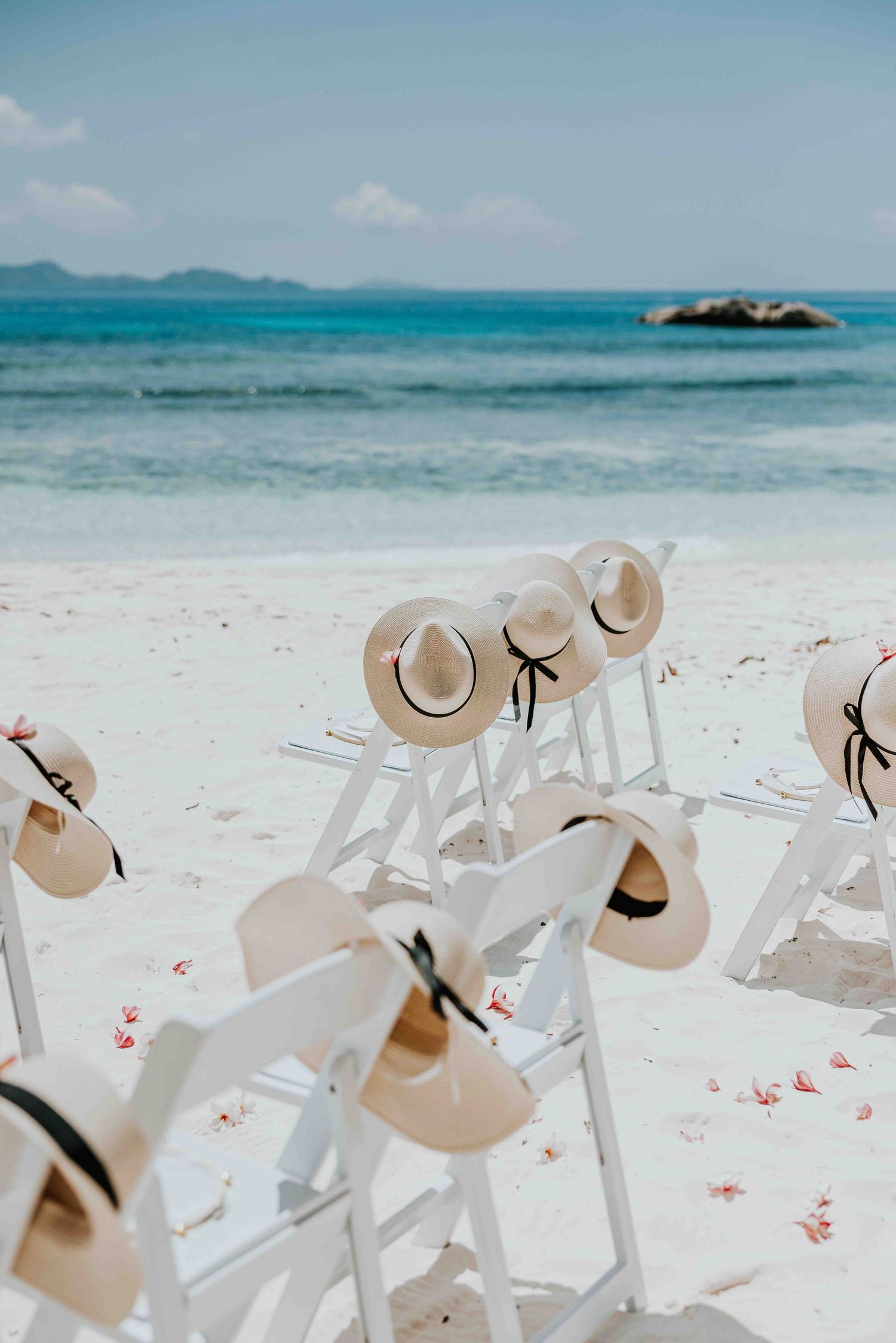 White chairs with straw hats on a tropical beach wedding setup with turquoise ocean backdrop.