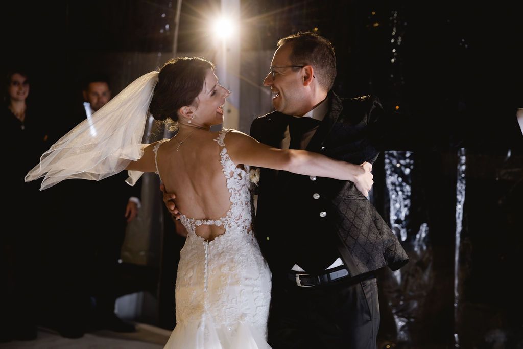 Bride and groom sharing an intimate first dance in a dramatic backlit outdoor evening setting.